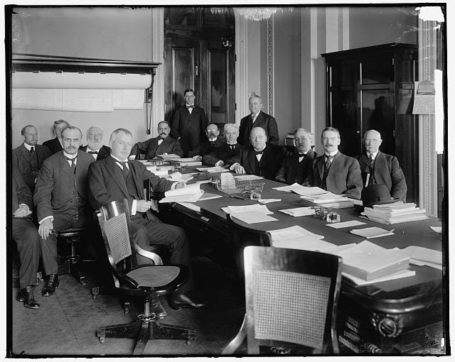 Members of the House Appropriations Committee seated around a conference table covered with documents and papers, photographed in 1905 by Harris & Ewing.